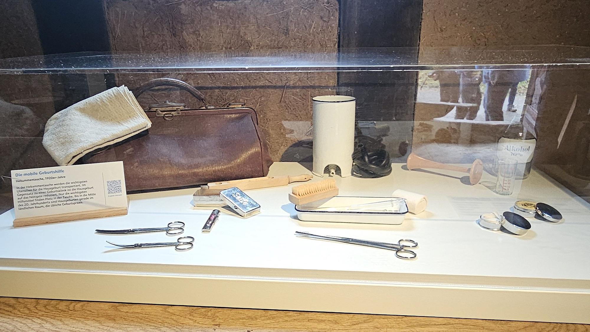 Blick in eine Vitrine mit einer Hebammentasche und einigen Utensilien.