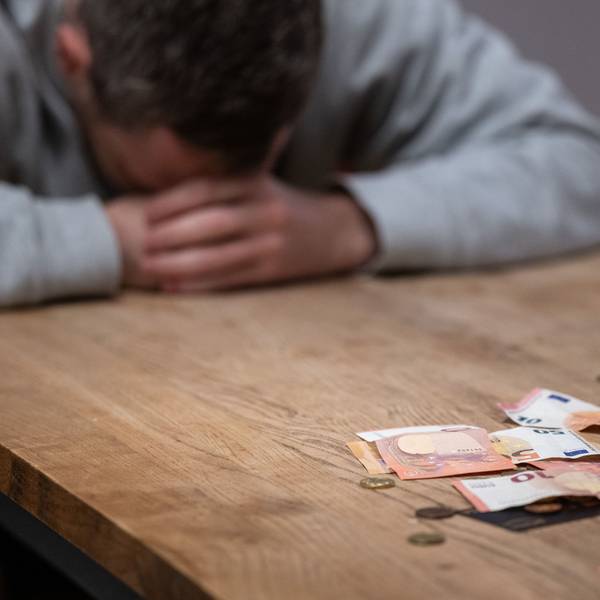 Das Bild zeigt einen Mann, der den Kopf auf den Tisch gelegt hat und offenbar Geldprobleme hat.