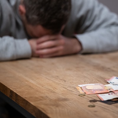 Das Bild zeigt einen Mann, der den Kopf auf den Tisch gelegt hat und offenbar Geldprobleme hat.