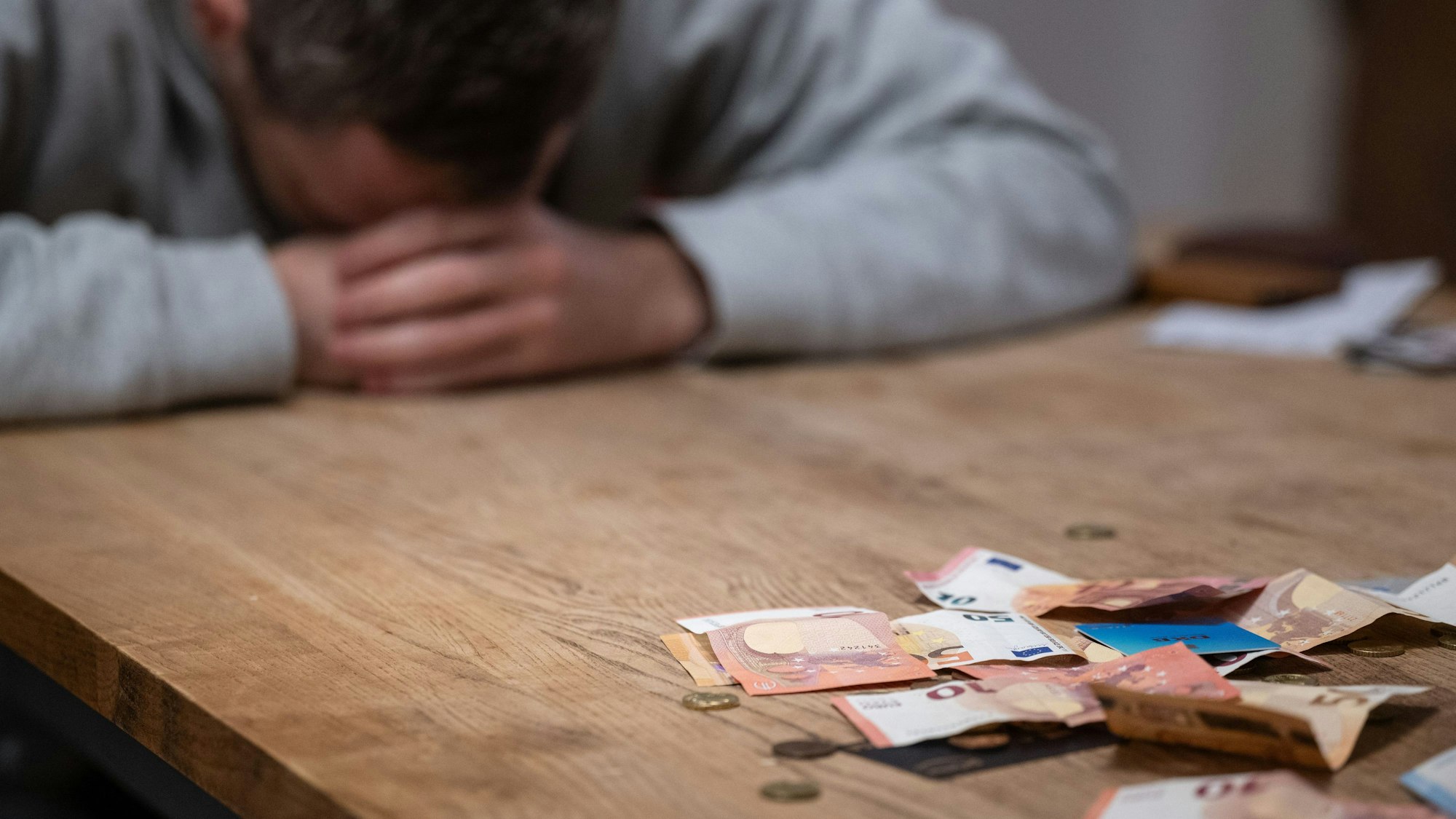 Das Bild zeigt einen Mann, der den Kopf auf den Tisch gelegt hat und offenbar Geldprobleme hat.