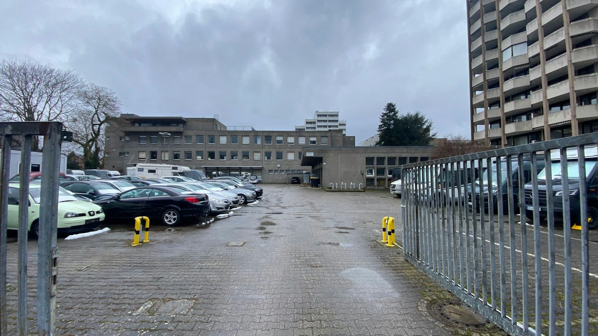 Zu sehen sind eine als Parkplatz genutzte Fläche sowie im Hintergrund Gebäude.