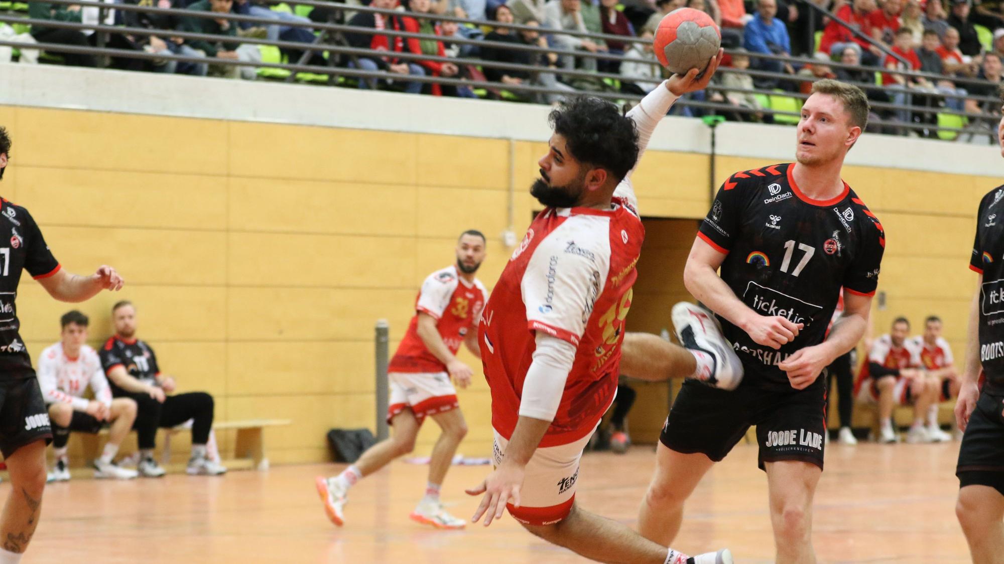 Ali Umat Sinaci liegt beim Wurf quer in der Luft, der Gegenspieler schaut in Richtung eigenes Tor.