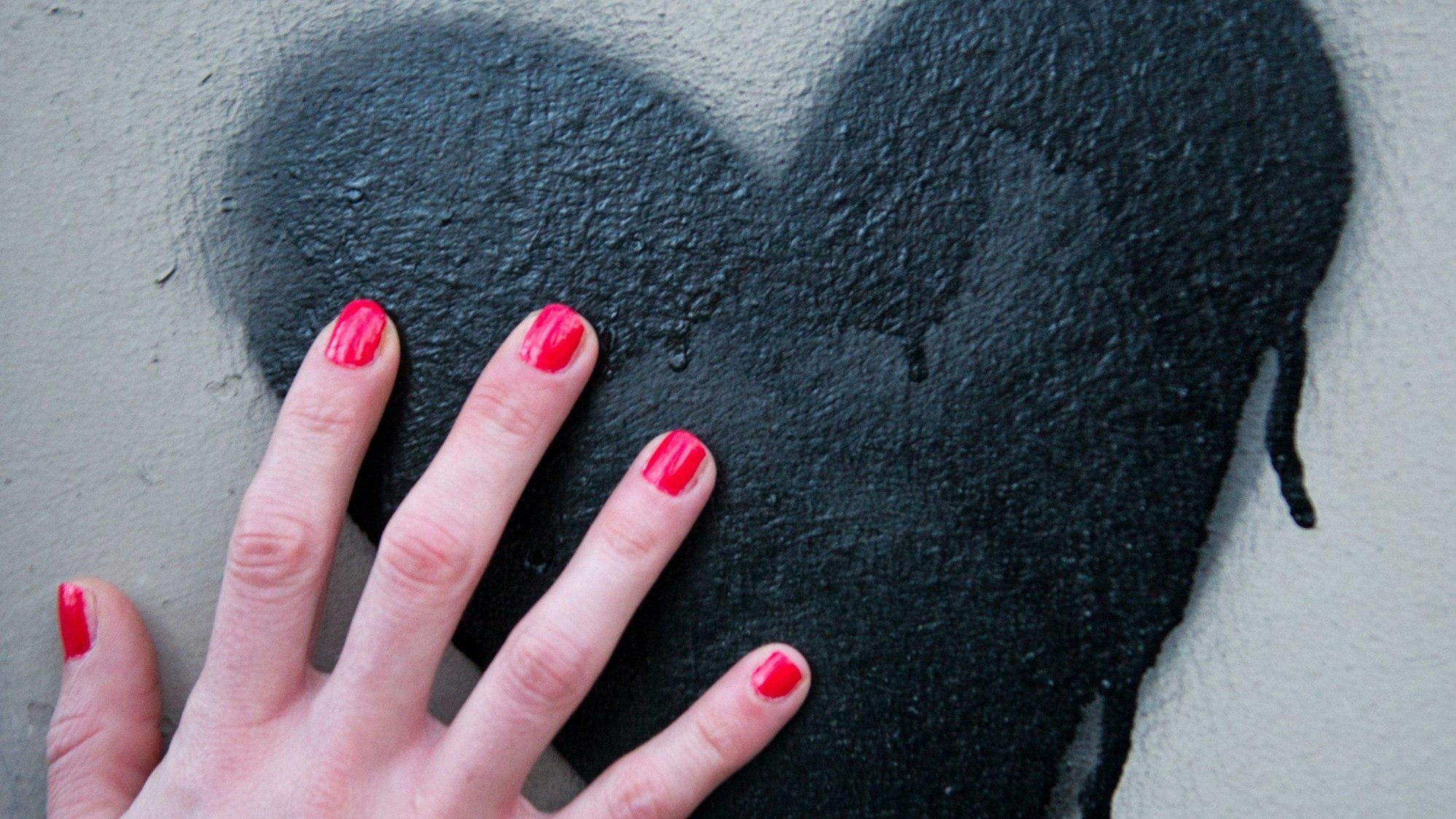 ARCHIV - ILLUSTRATION - Eine Frauenhand mit rot lackierten Fingernägeln berührt am 03.03.2014 in Berlin ein Herz, das auf eine Mauer gesprüht wurde. Foto: Inga Kjer/dpa (zu dpa "Herzinfarkt ist nicht nur Männersache - Das Frauenherz tickt anders") +++(c) dpa - Bildfunk+++