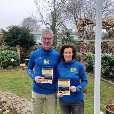 Ein Mann und eine Frau stehen nebeneinander in einem Garten. Sie halten Flyer zum Nachtlauf in der Hand.