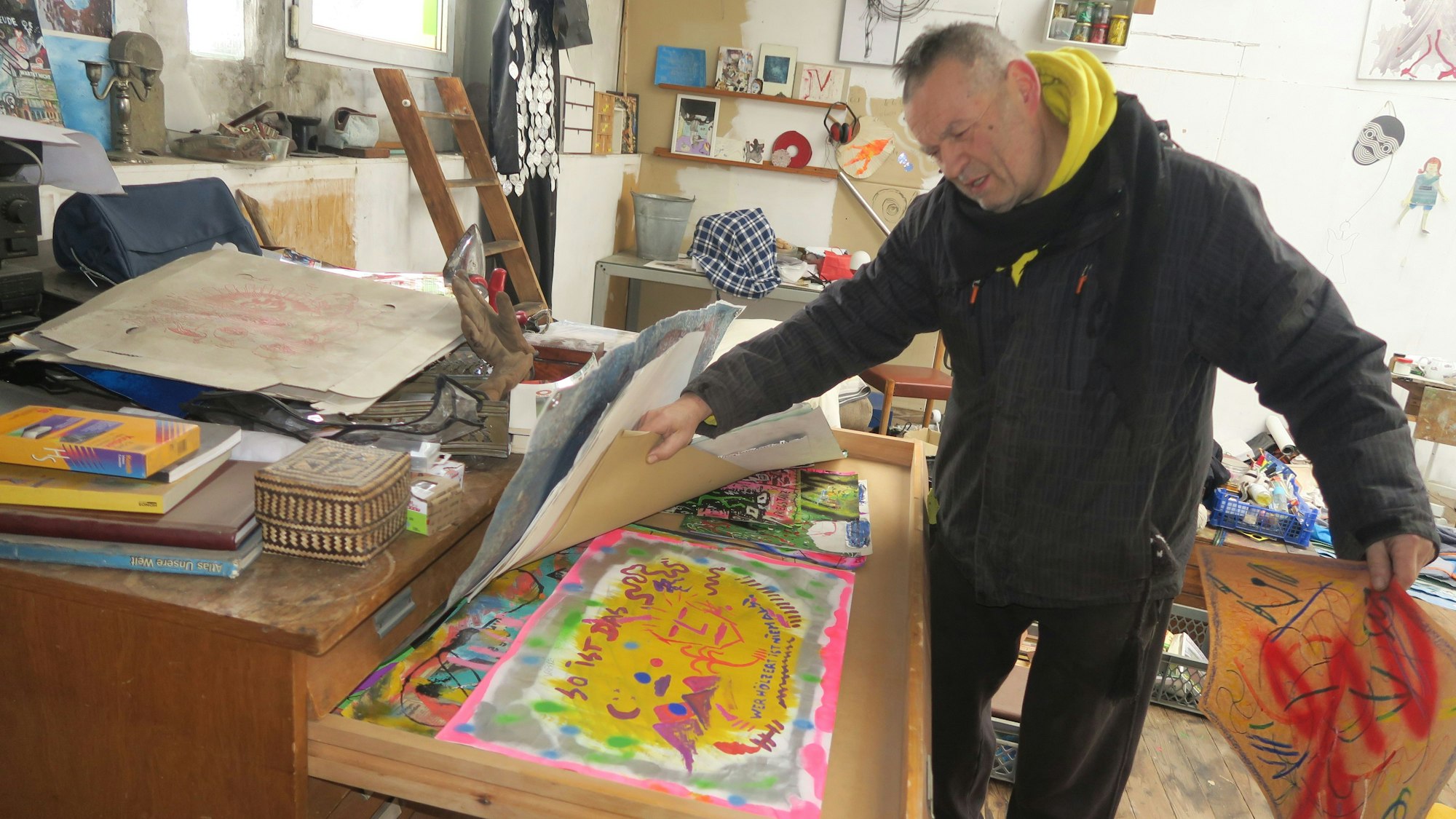 Ein Mann hat in einer großen Schublade ein sehr buntes Bild gefunden.