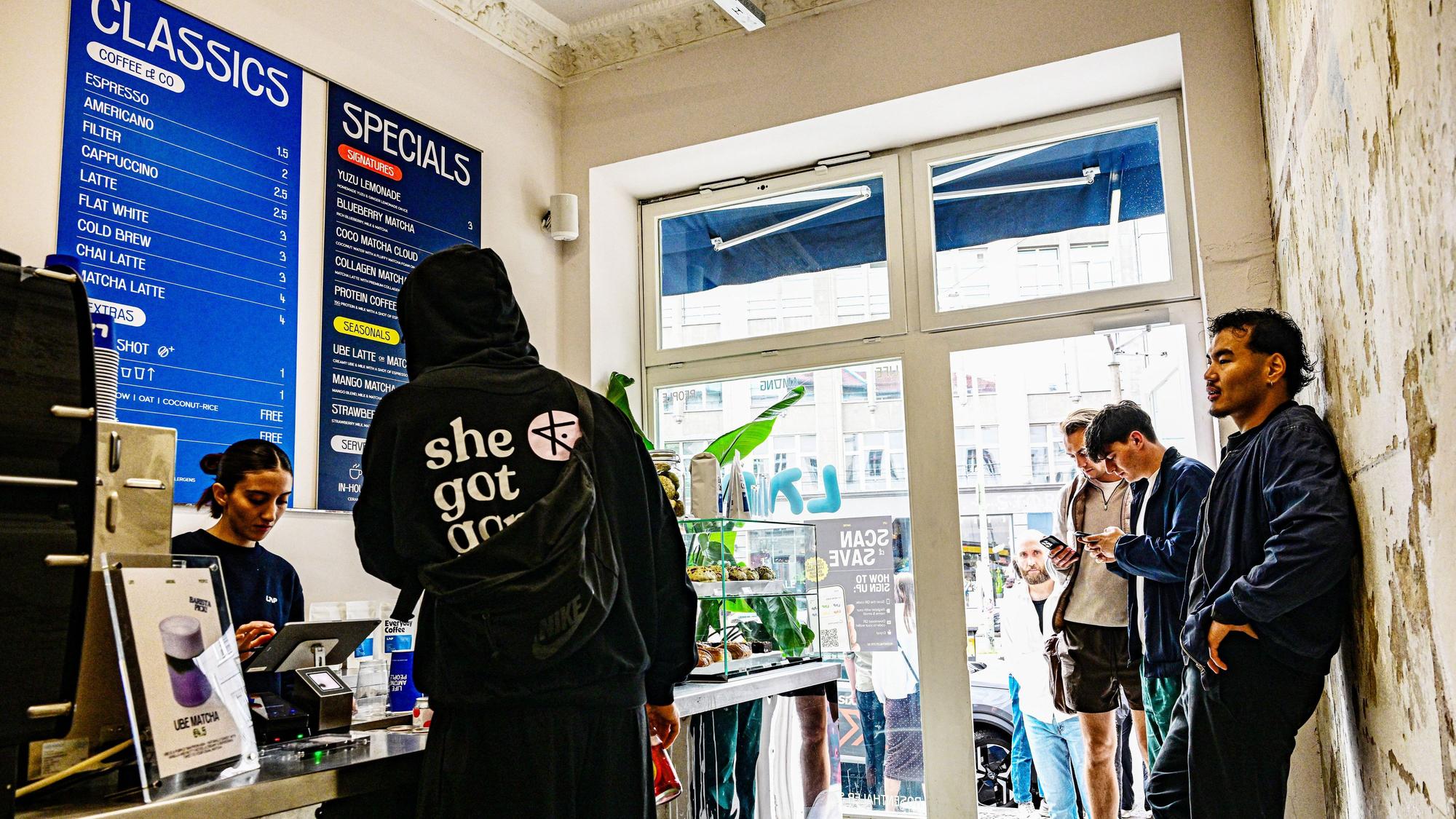Vier junge Leute stehen in einem kleinen Verkaufsraum und warten auf ihren Kaffee.