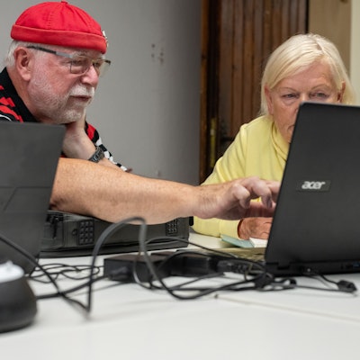 Ein Mann und eine Frau sitzen an einem Tisch, vor ihnen stehen Laptops.