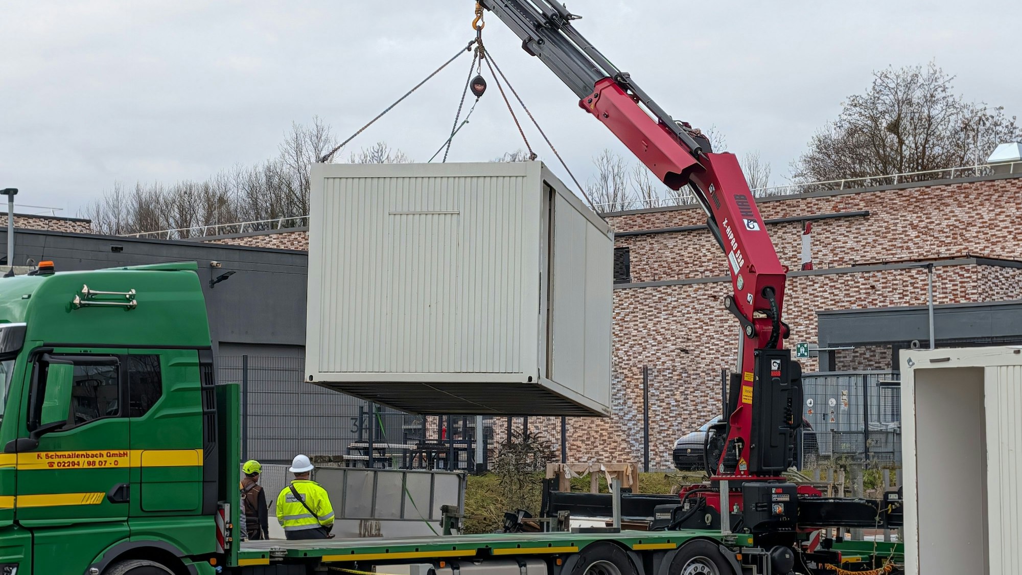 Das Foto zeigt die Verladung eines Baustellencontainers mit einem Autokran.