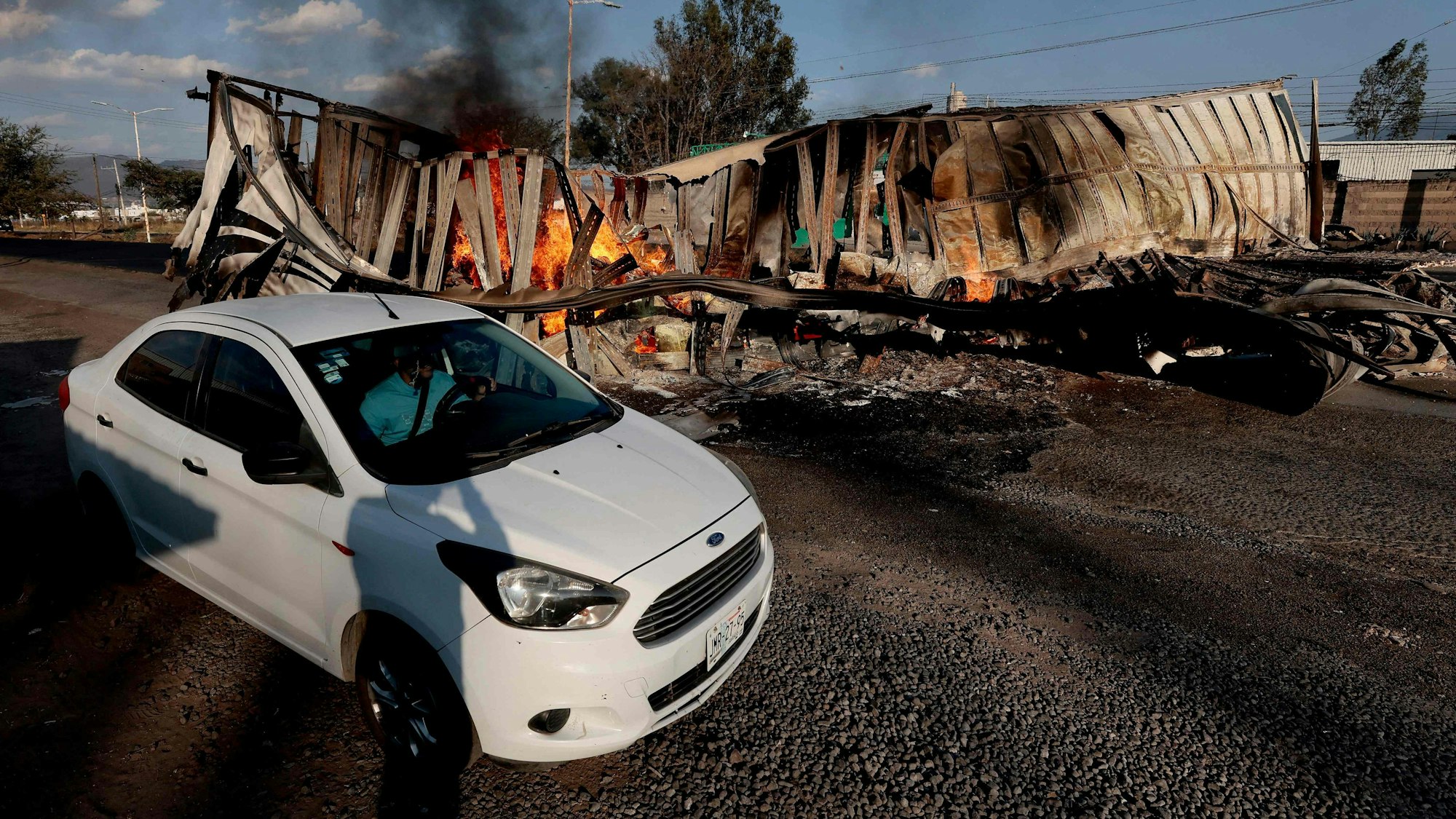 Acatlan de Juarez: Ein Auto fährt an einem ausgebrannten Lastwagen vorbei, der von Drogenkartellen in Brand gesetzt wurde.