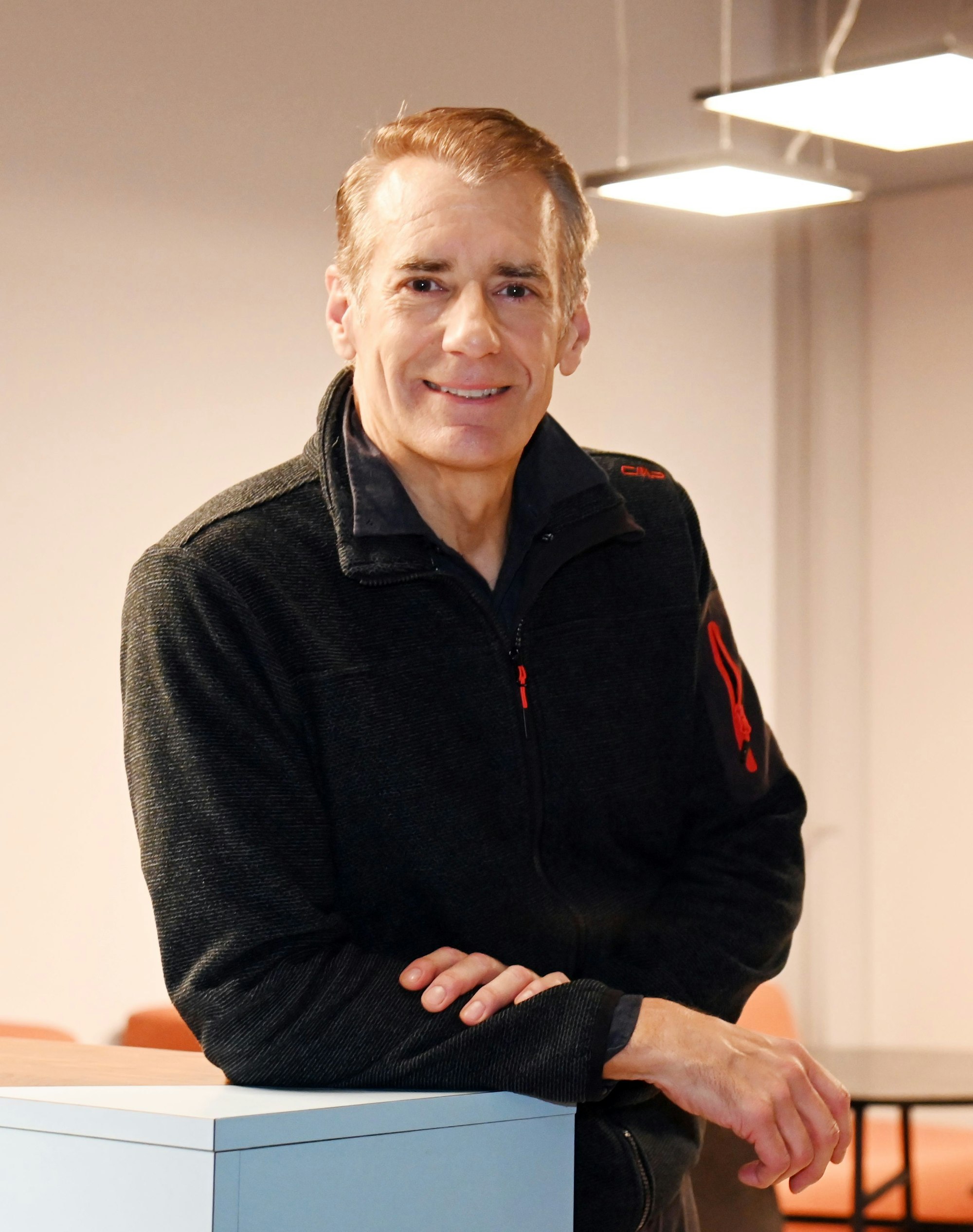 Ein Mann mit grauem Haar und schwarzem Pullover steht an einem Tisch.