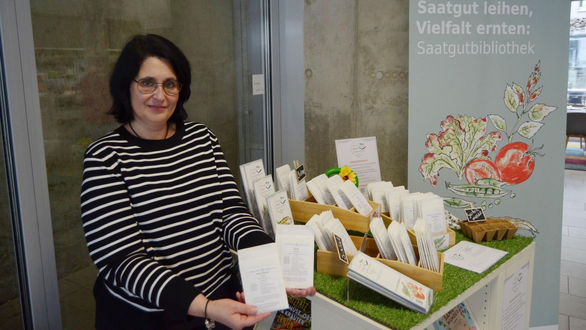 Die Mitarbeiterin steht neben einem Tisch mit Saatgut-Tüten und Infoblättern.