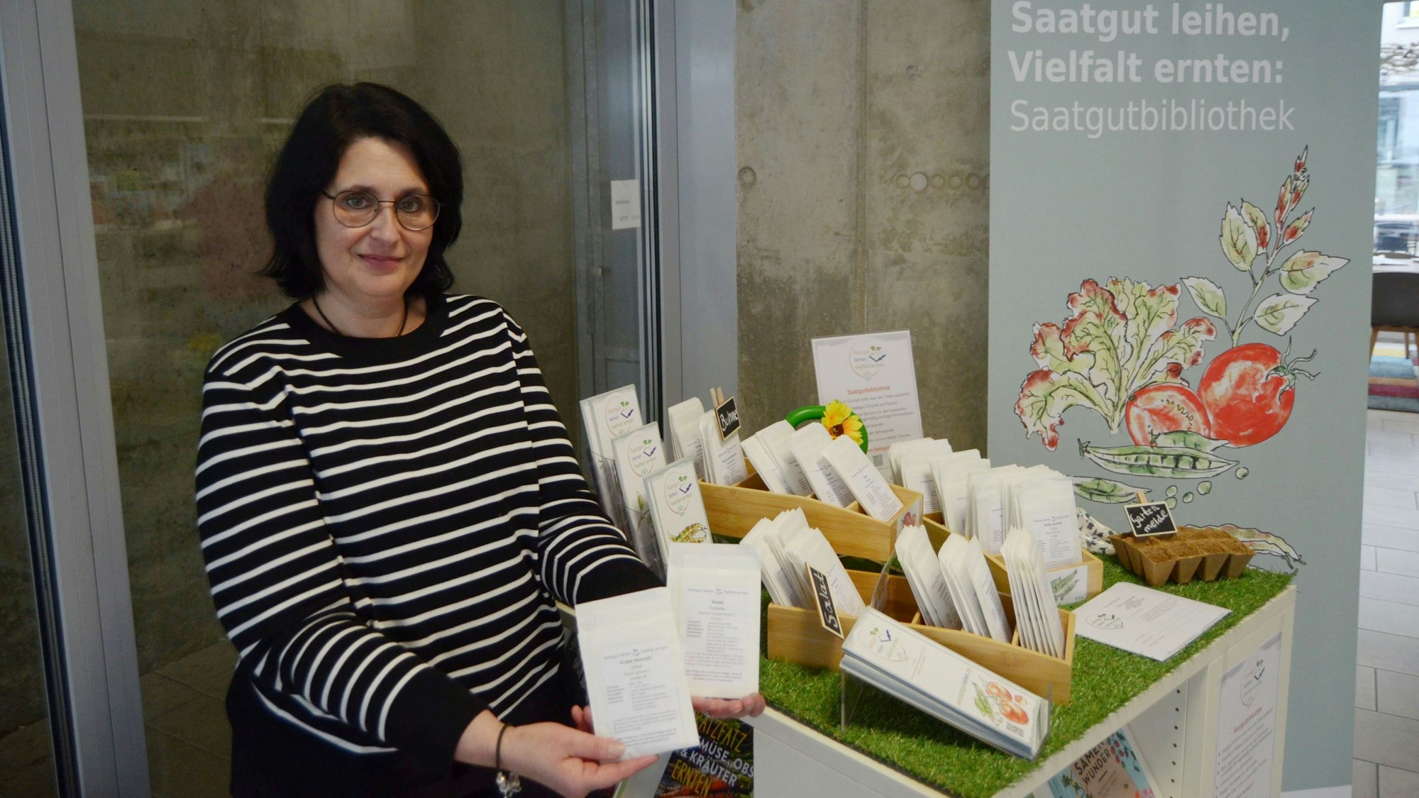 Die Mitarbeiterin steht neben einem Tisch mit Saatgut-Tüten und Infoblättern.