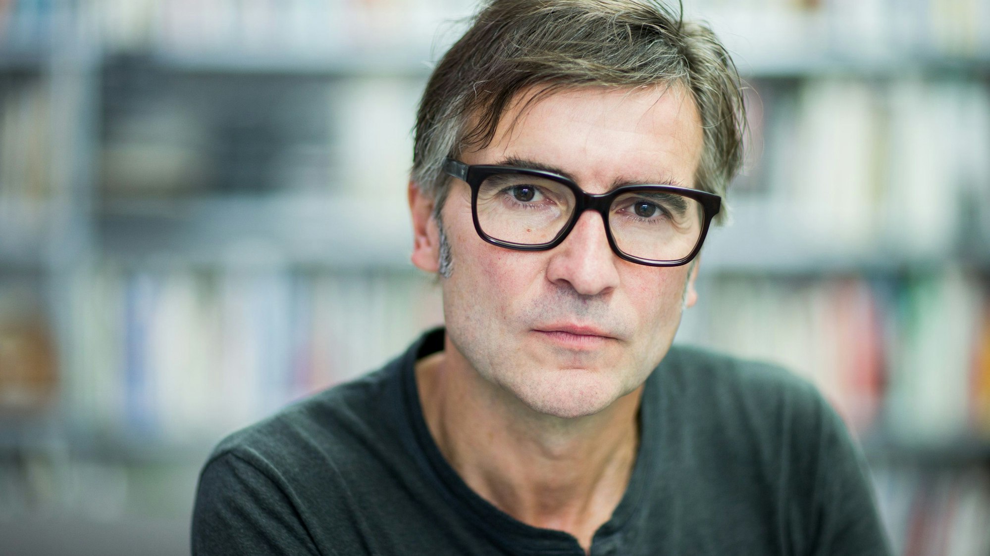 Ein Mann mit schwarz gerahmter Brille blickt ernst in die Kamera.