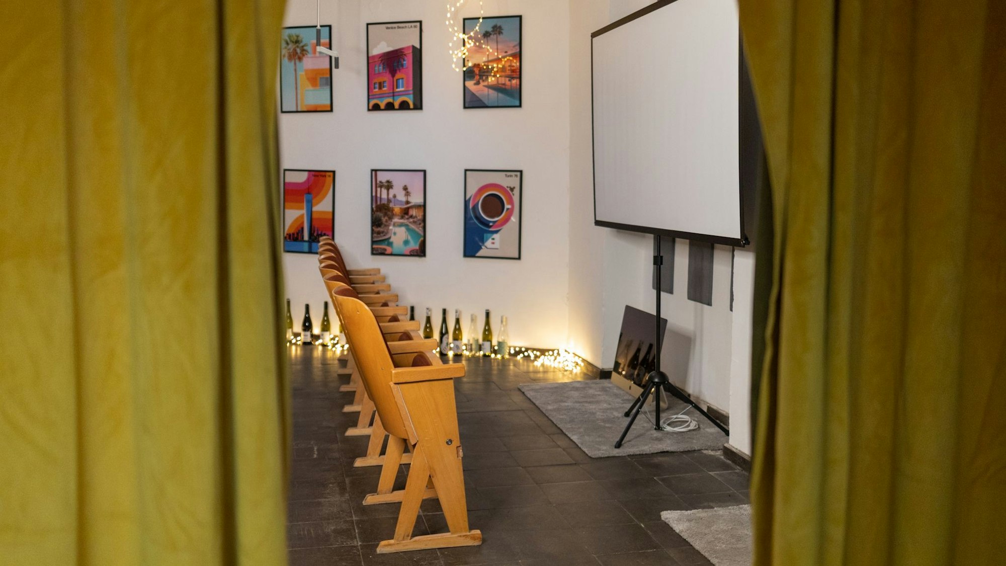 Blick auf Kinostühle aus Holz vor einer Leinwand.