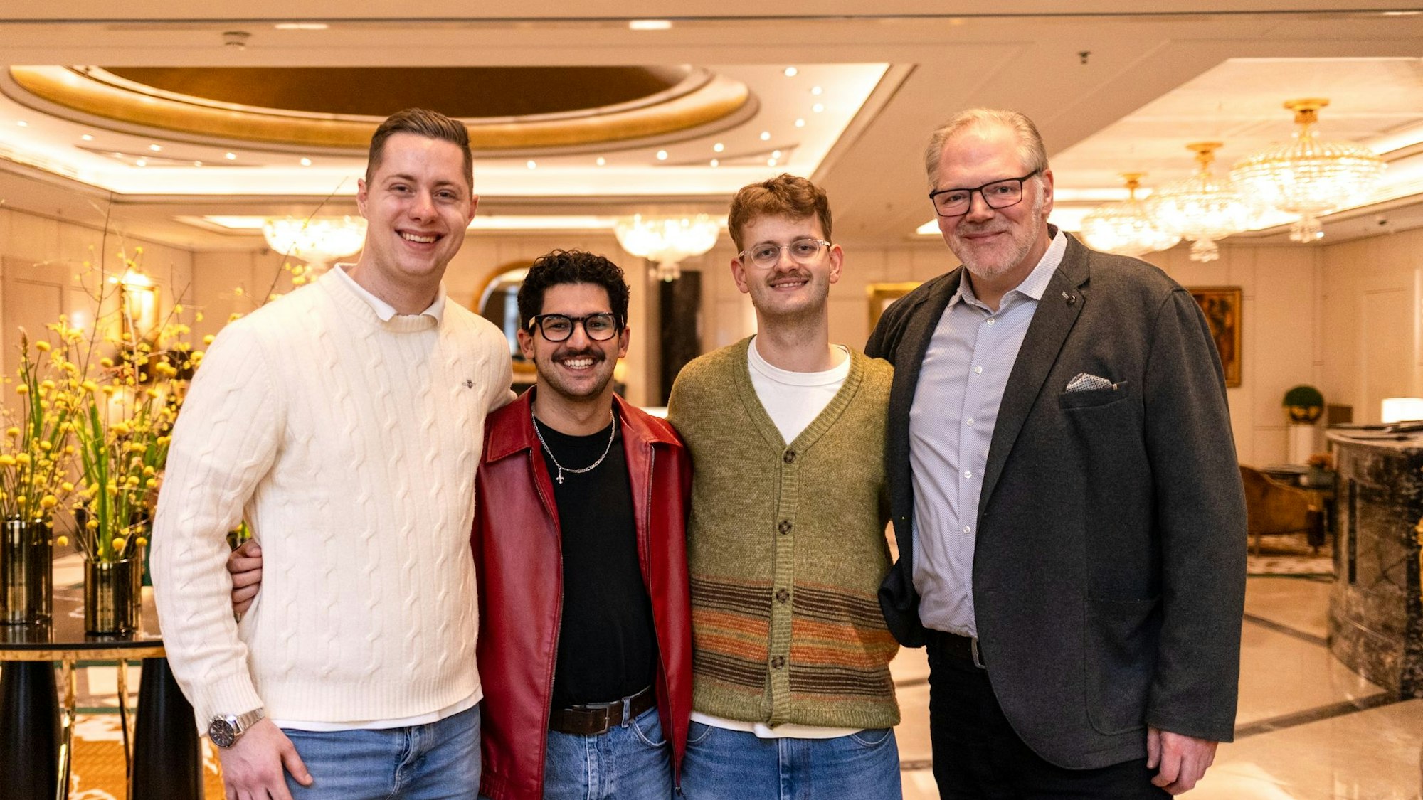 Vier Männer stehen Arm in Arm in einer Hotellobby.