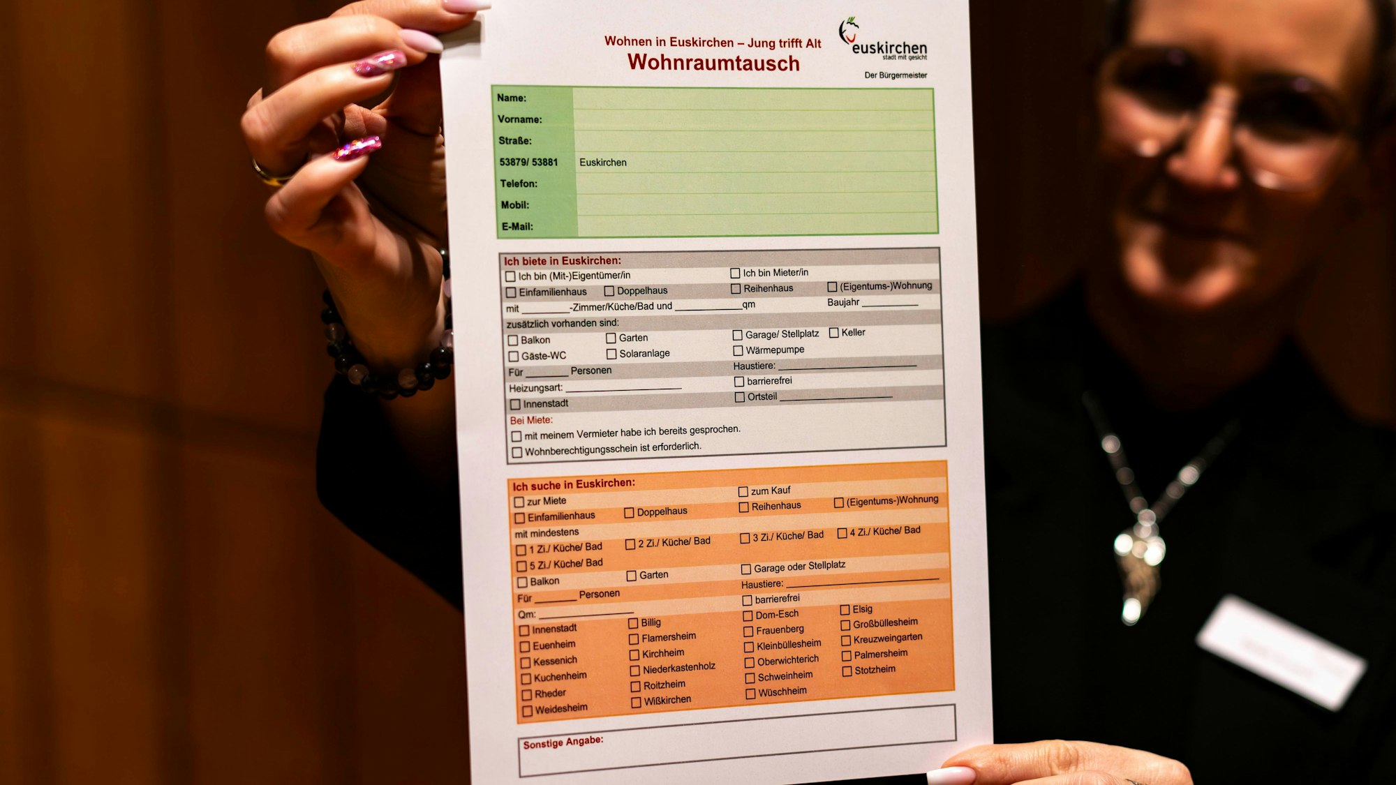 Eine Frau ist unscharf im Hintergrund zu erkennen. Sie hält den Vordruck für den Wohnraumtausch in Euskirchen in die Kamera.