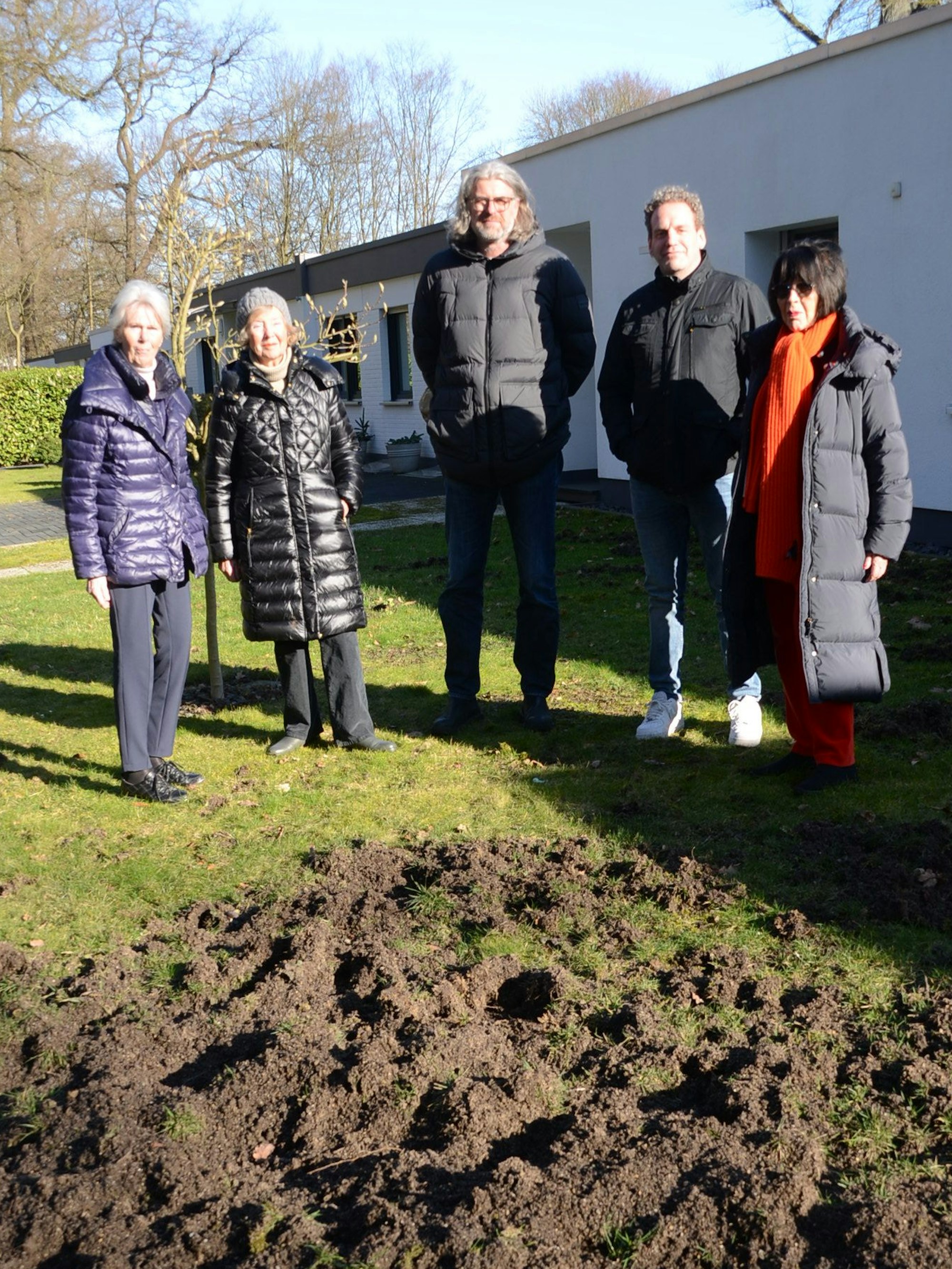 Männer und Frauen in einem Vorgärten vor einer von Tieren zerwühlten Rasenfläche.