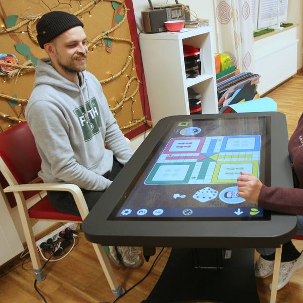Auf dem Bild sind eine Frau und ein Mann zu sehen, die an einem digitalen Spieltisch sitzen.