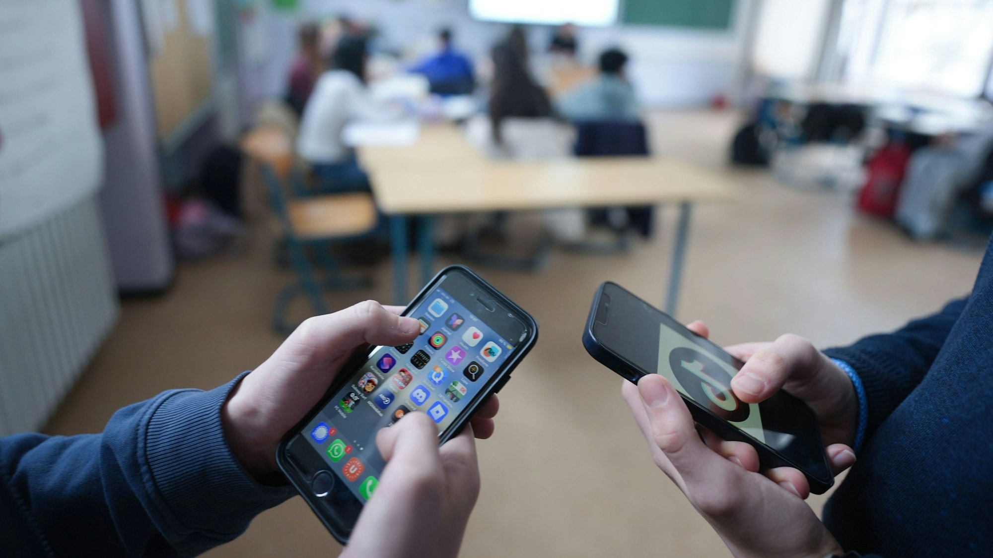 Zwei Schüler stehen in einem Klassenraum und schauen auf ihre Smartphones.