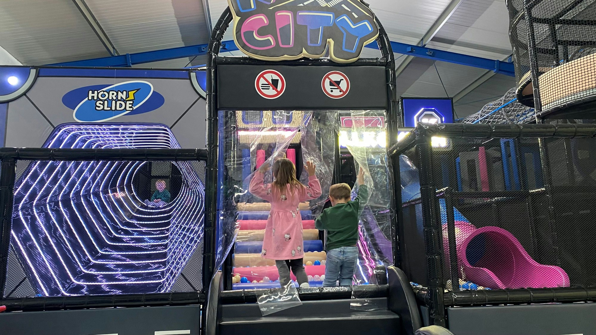 Zu sehen sind zwei kleine Kinder, die in ein Bällebad steigen.