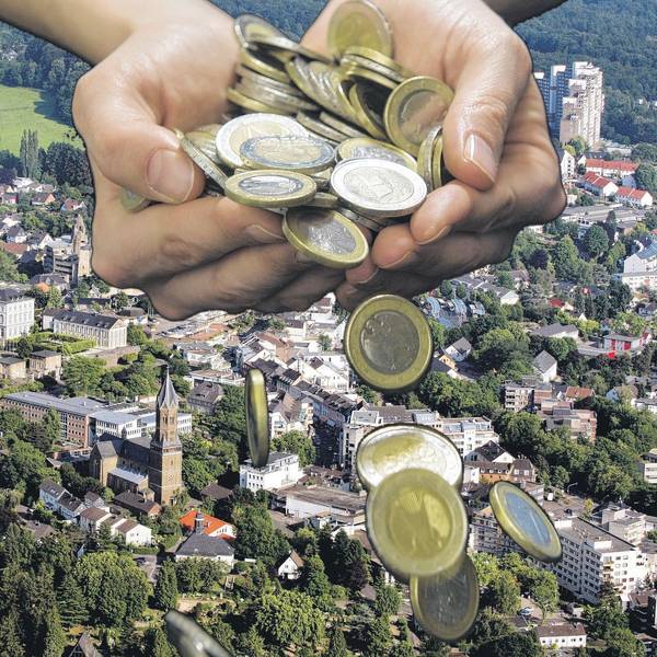 Aus einer Hand fallen Geldmünzen auf ein Stadtpanorama