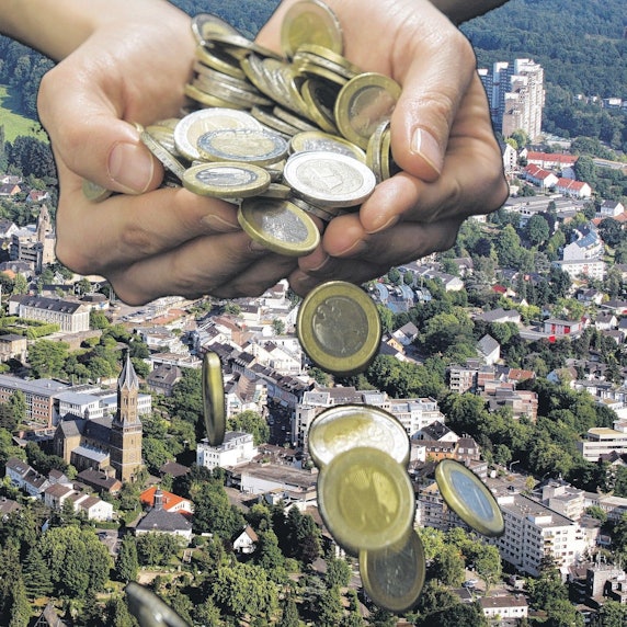 Aus einer Hand fallen Geldmünzen auf ein Stadtpanorama