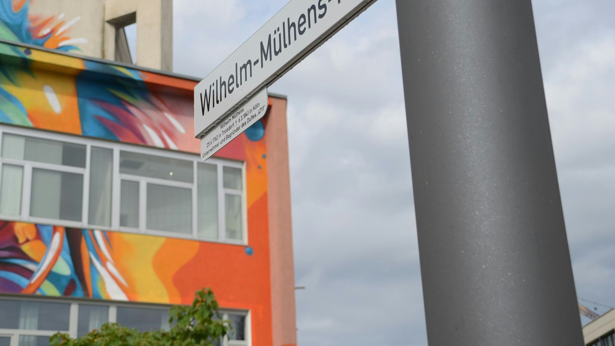 Ein bunt gemaltes Gebäude und ein Straßenschild "Wilhelm-Mülhens-Platz".