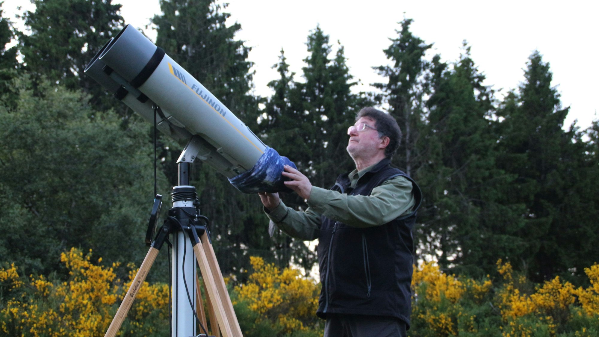 Der Astronom steht an einem großen Teleskop, das im Freien auf einem Stativ steht und auf den Himmel gerichtet ist.