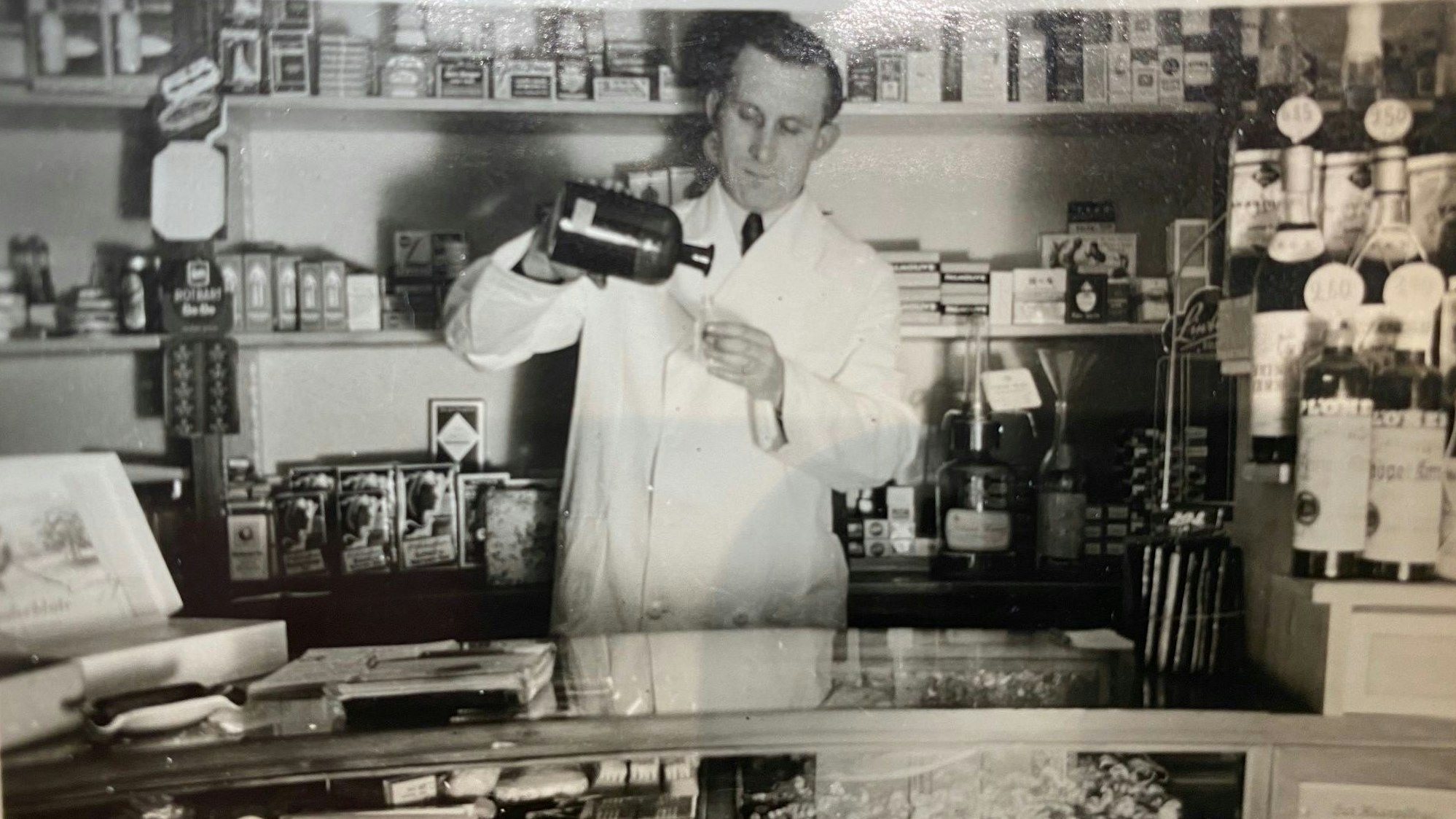 Zu sehen ist eine Schwarz-weiß-Aufnahme, die den Großvater bei der Arbeit in der Drogerie zeigt.