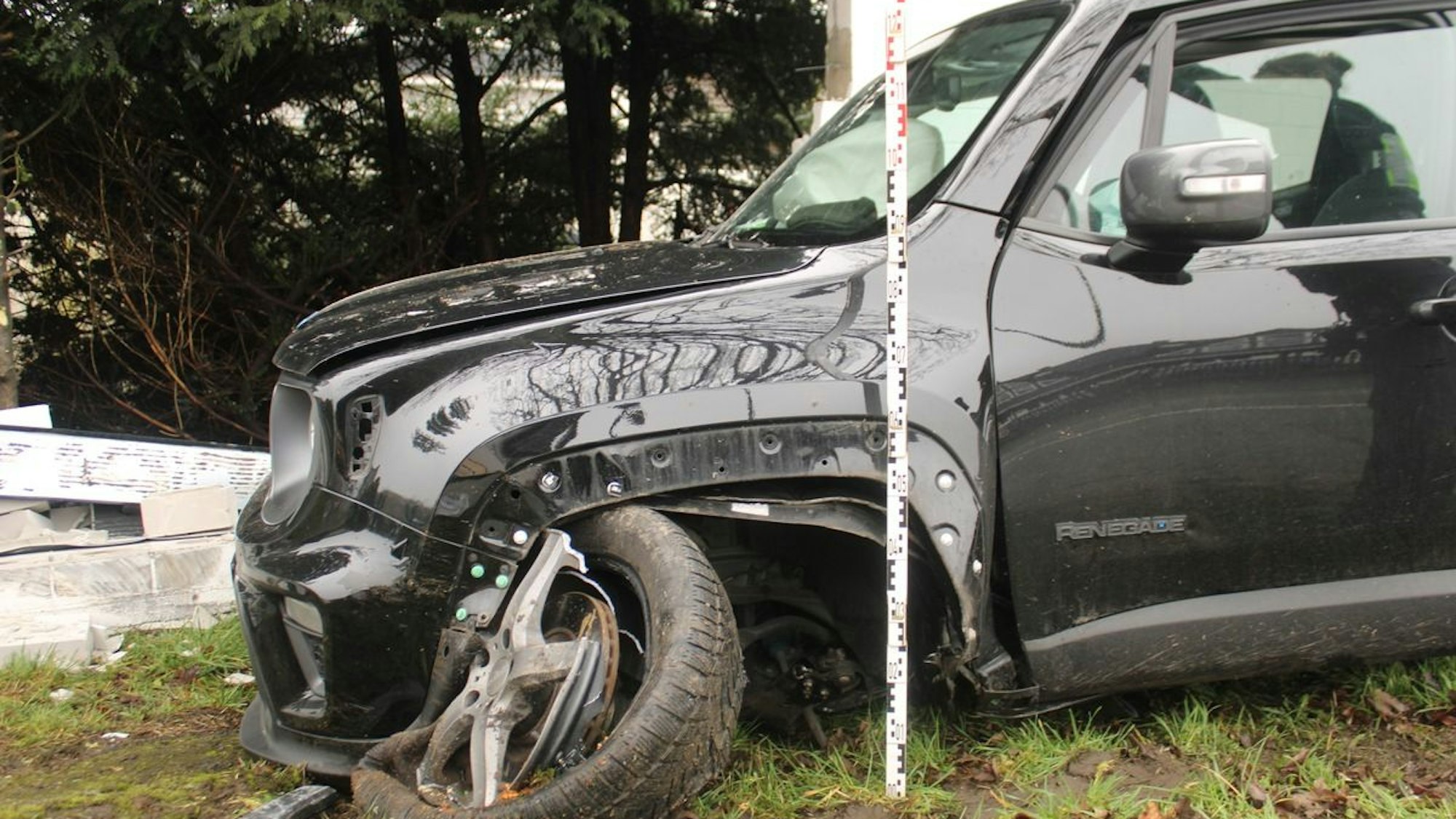 Ein schwer beschädigtes Auto ist zwischen einem Baum und einer Mauer eingeklemmt.