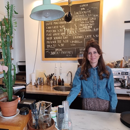 Eine Frau mit langen dunklen Haaren steht hinter der Theke eines Cafés.