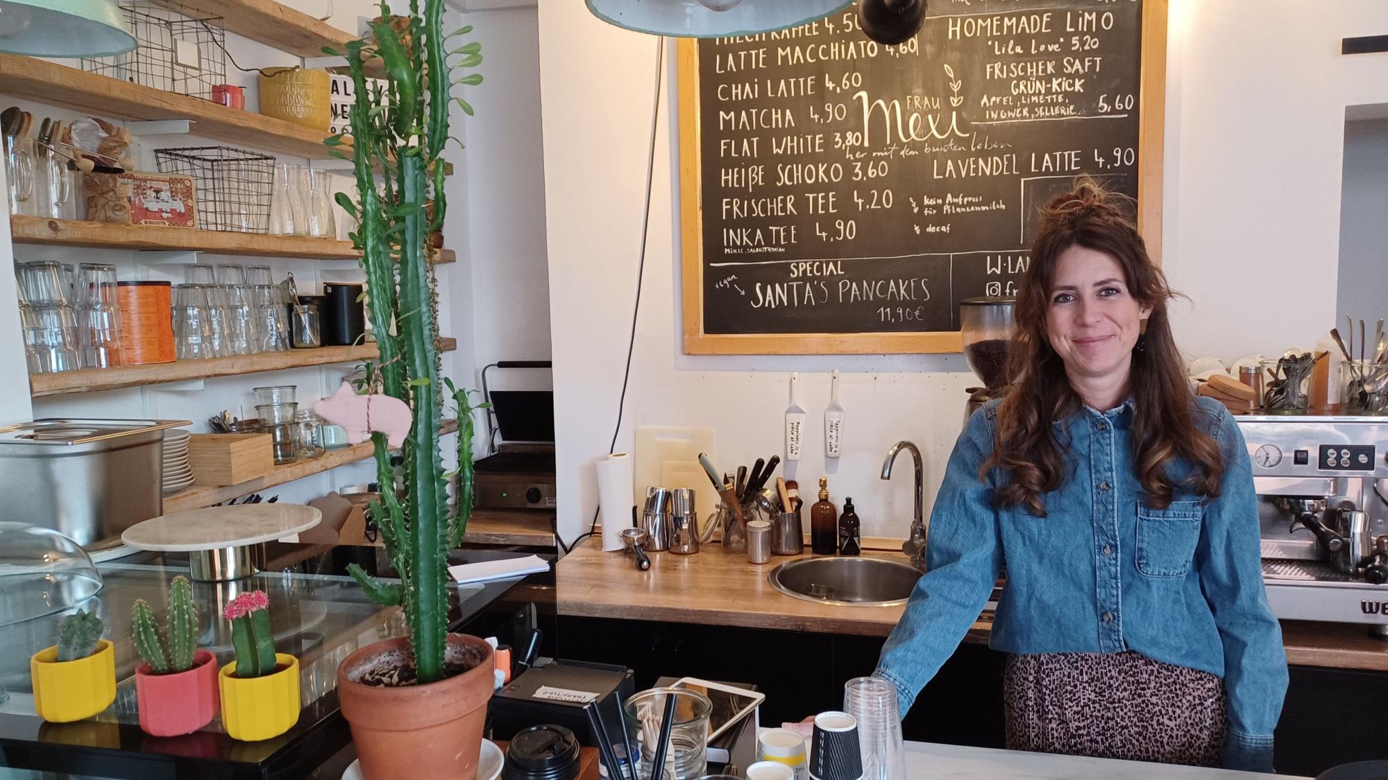 Eine Frau mit langen dunklen Haaren steht hinter der Theke eines Cafés.