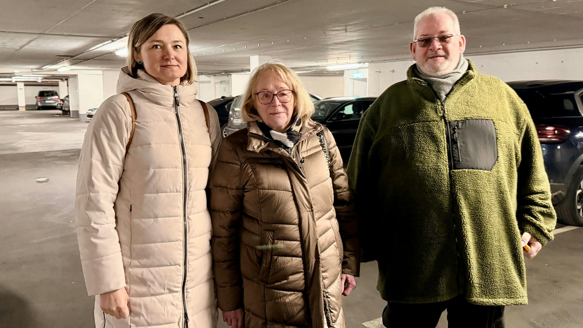 Die beiden Frauen von der Eigentümergemeinschaft und der Hausmeister stehen nebeneinander in der Tiefgarage und blicken in die Kamera.