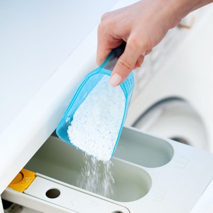 Ein Waschmaschinenfach ist auf und jemand kippt Waschpulver hinein.