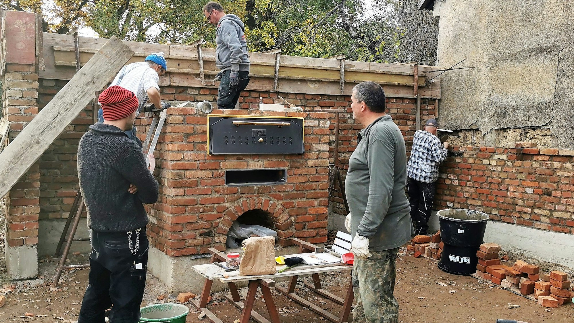 Fünf Männer arbeiten an einem gemauerten Backofen.
