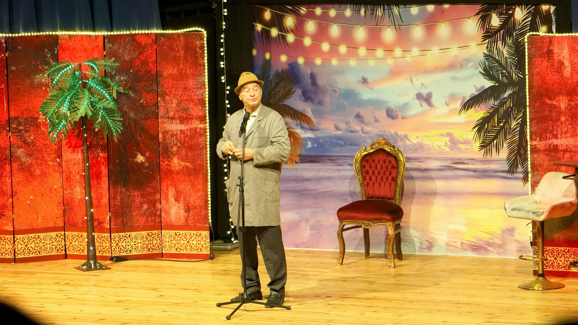 Gerhardt steht im Hausmeisterkittel und mit Hut auf der Theaterbühne.