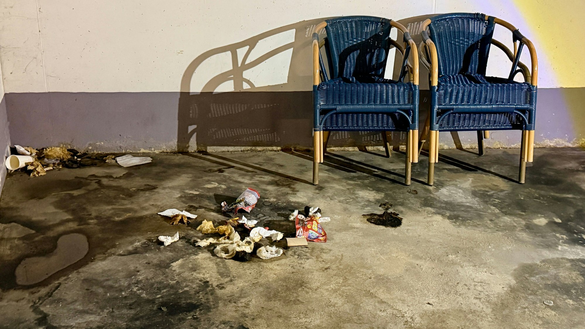 Zwei blaue Korbstühle stehen nebeneinander, der Boden davor ist fleckig und voller Abfälle.