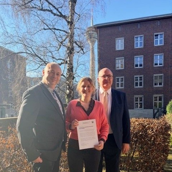 Zwei Männer und eine Frau stehen im Gegenlicht.