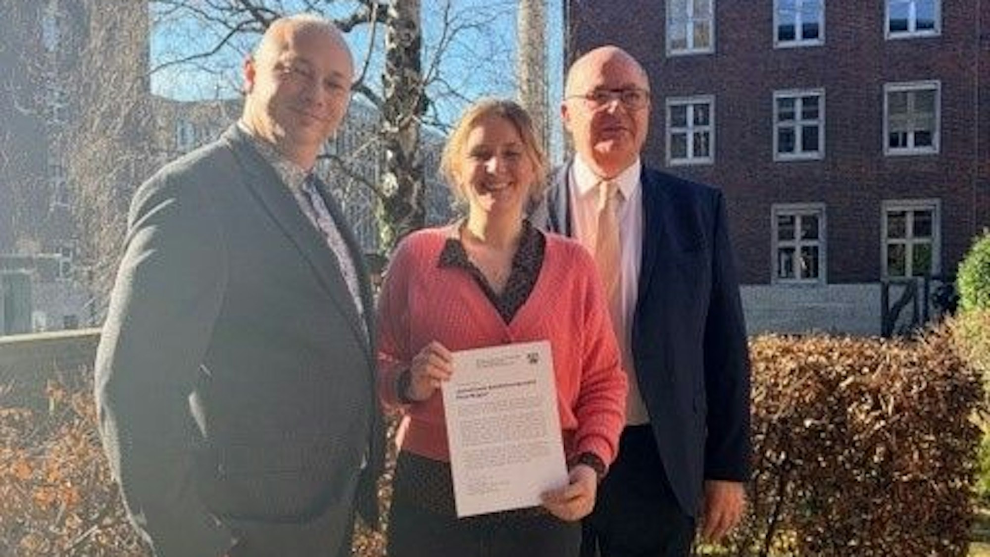 Zwei Männer und eine Frau stehen im Gegenlicht.