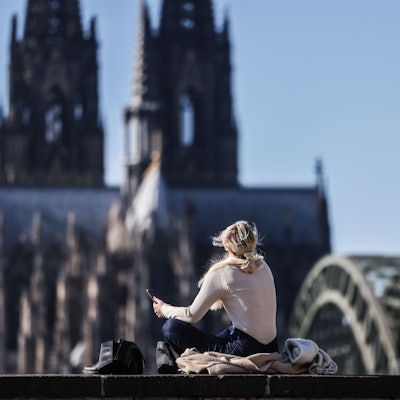 Eine Frau blickt am Rheinufer in Köln vor dem Dom in den Himmel.