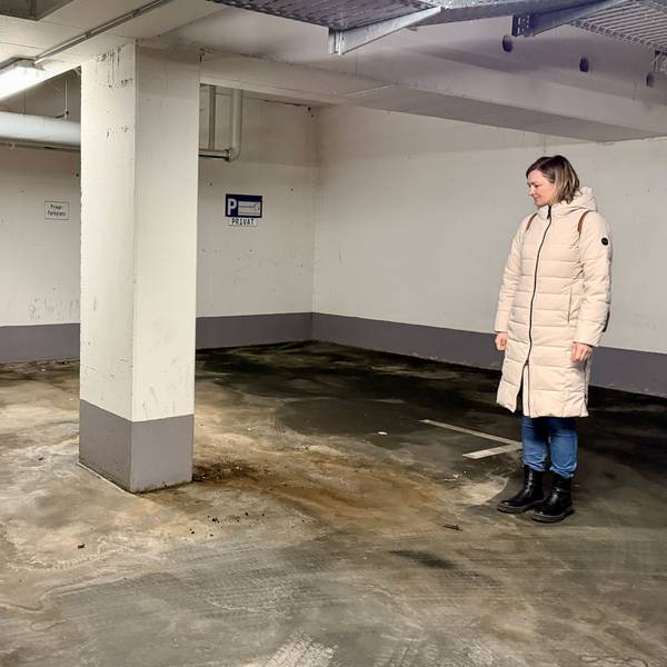 Eine Frau aus der Eigentümergemeinschaft steht im Parkhaus und blickt auf den Boden.