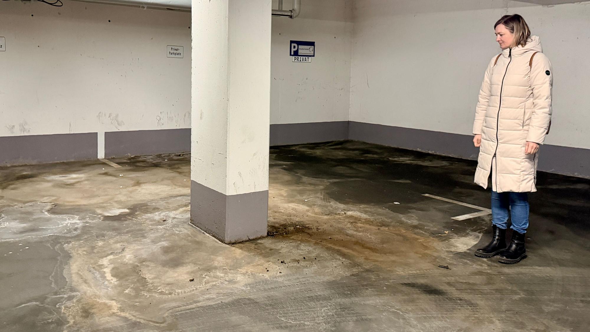 Eine Frau aus der Eigentümergemeinschaft steht im Parkhaus und blickt auf den Boden.