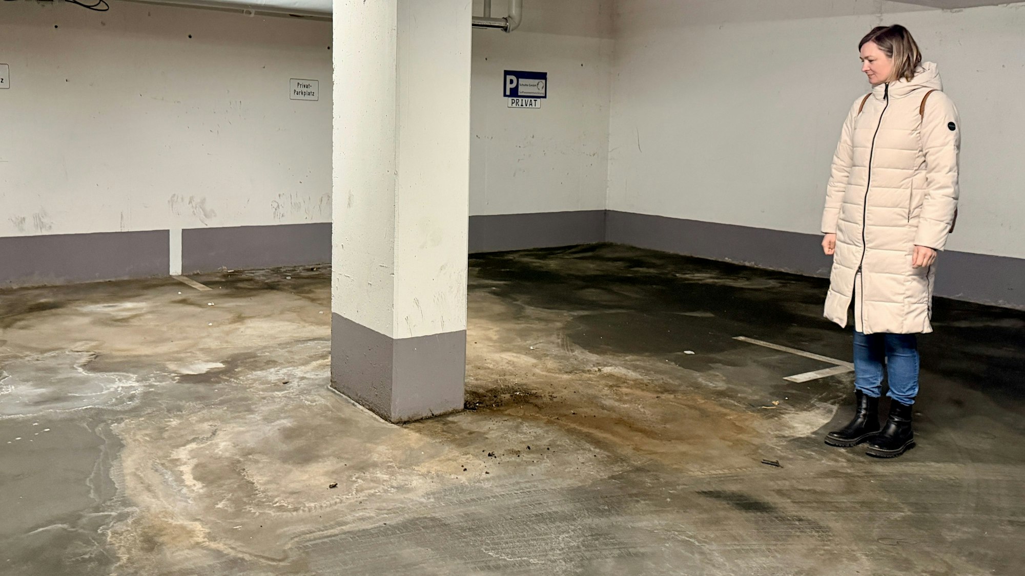 Eine Frau aus der Eigentümergemeinschaft steht im Parkhaus und blickt auf den Boden.