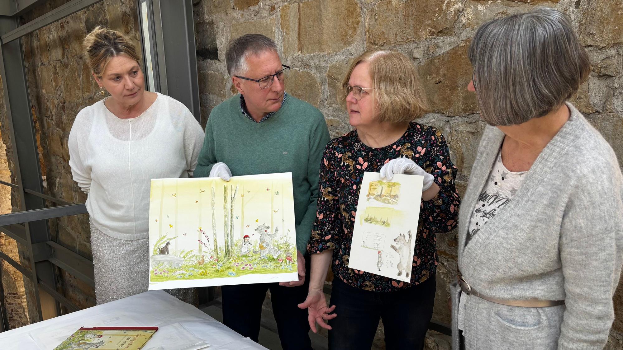 Drei Frauen und ein Mann stehen nebeneinander und halten bunte Illustrationen von Sebastian Meschenmoser in der Hand.