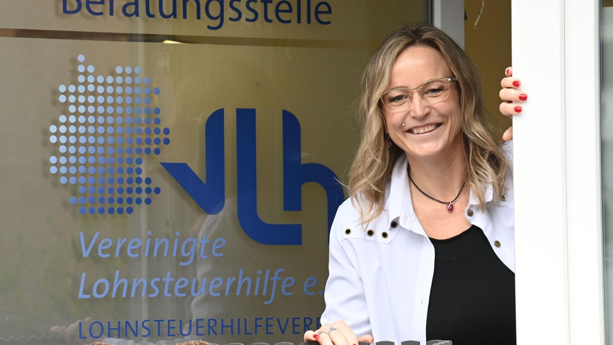 Anke Pfeilsticker lehnt sich aus dem Fenster ihrer Beratungsstelle. Auf der Scheibe steht „Beratungsstelle, VLH, Vereinigte Lohnsteuerhilfe“
