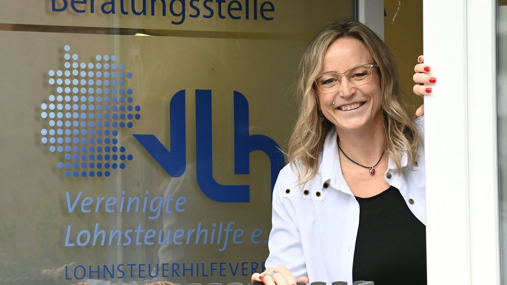 Anke Pfeilsticker lehnt sich aus dem Fenster ihrer Beratungsstelle. Auf der Scheibe steht „Beratungsstelle, VLH, Vereinigte Lohnsteuerhilfe“