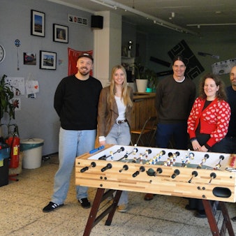 Einige junge Frauen und Männer stehen um einen Kicker herum.