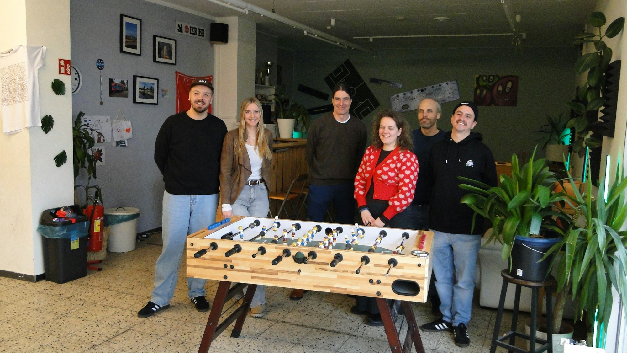 Einige junge Frauen und Männer stehen um einen Kicker herum.