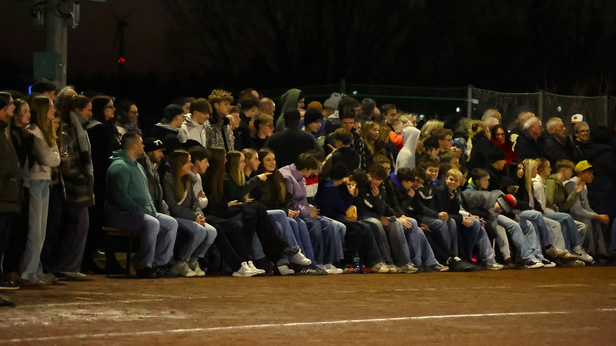Zahlreiche Zuschauer sitzen und stehen am Spielfeldrand.