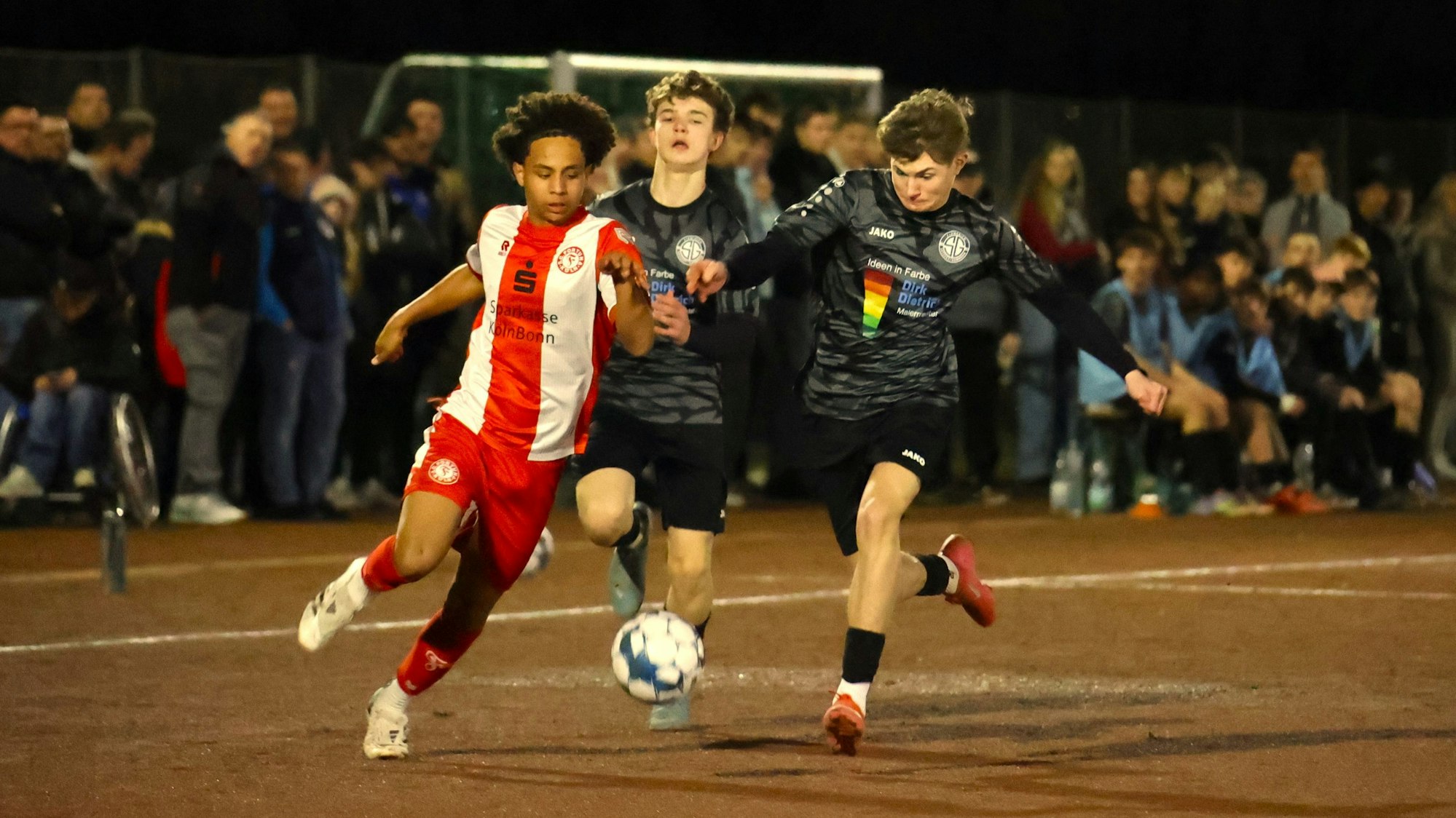 Laufduell zwischen einem Kölner und einem JSG-Spieler unweit der Außenlinie. Ein weiterer JSG-Spieler kommt nicht hinterher.